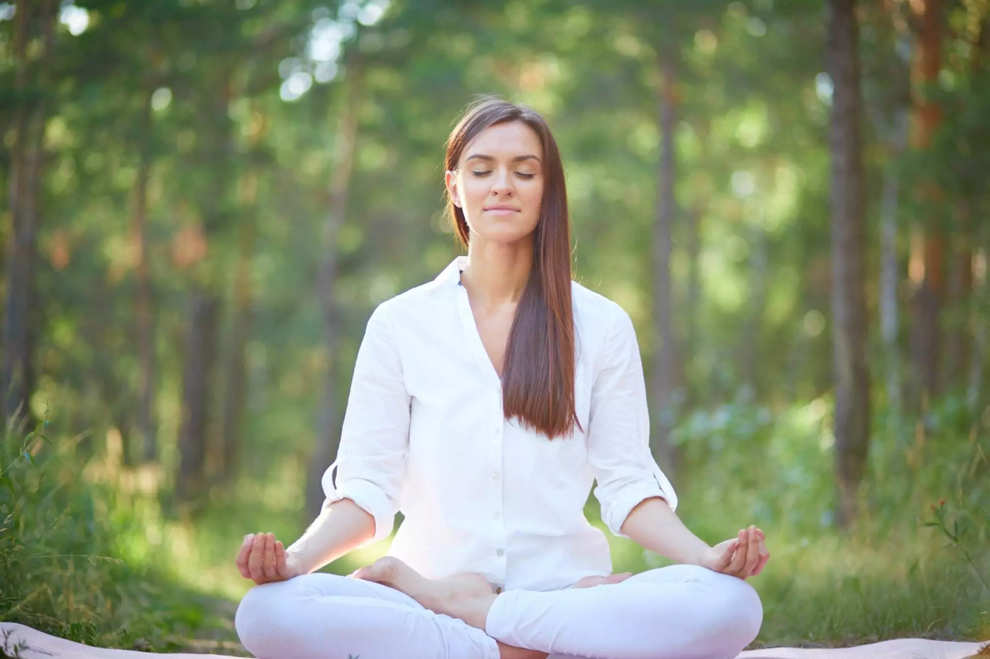 Woman meditating peacefully in sunlit forest.