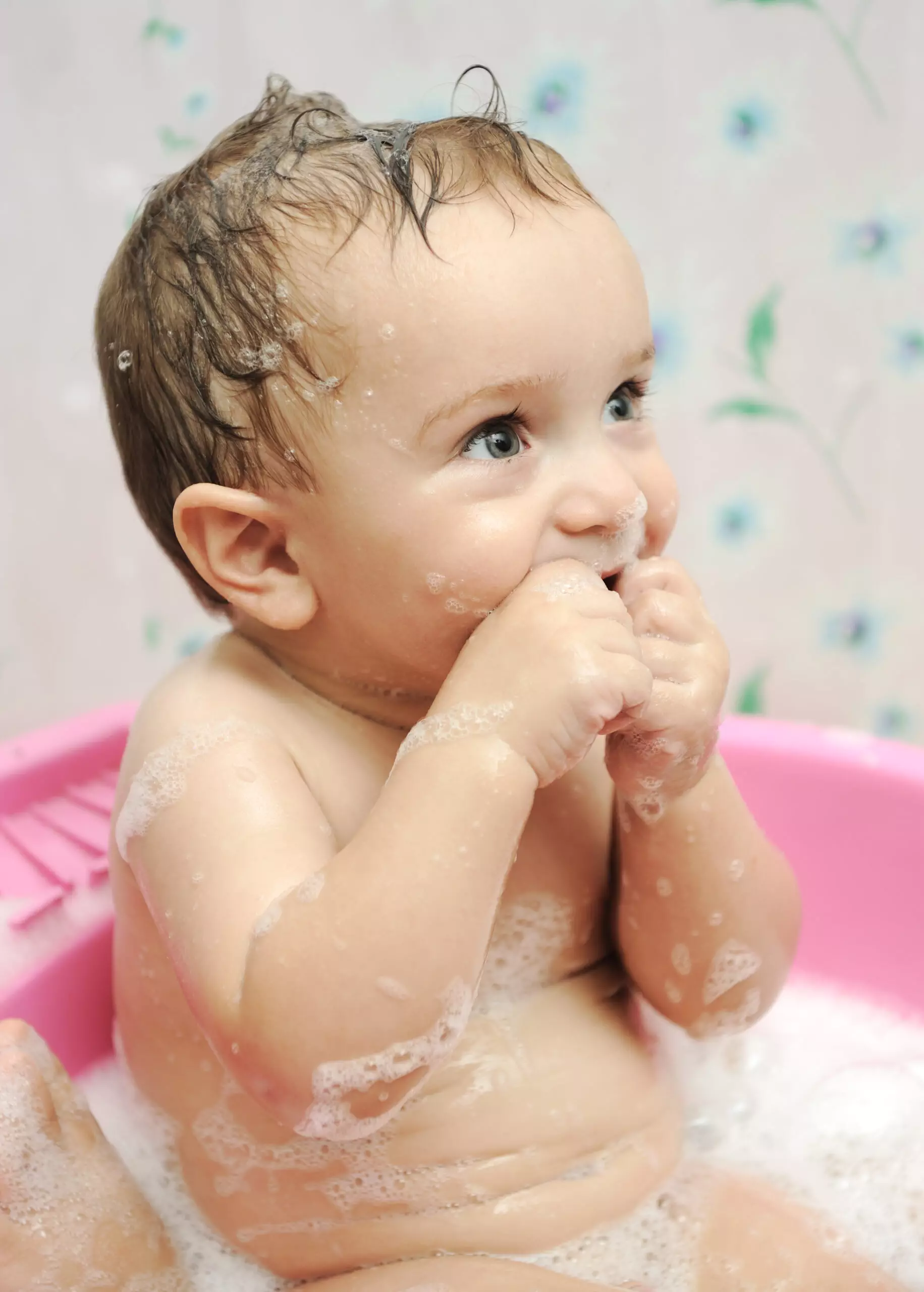 Baby bathing in pink tub with soap bubbles.