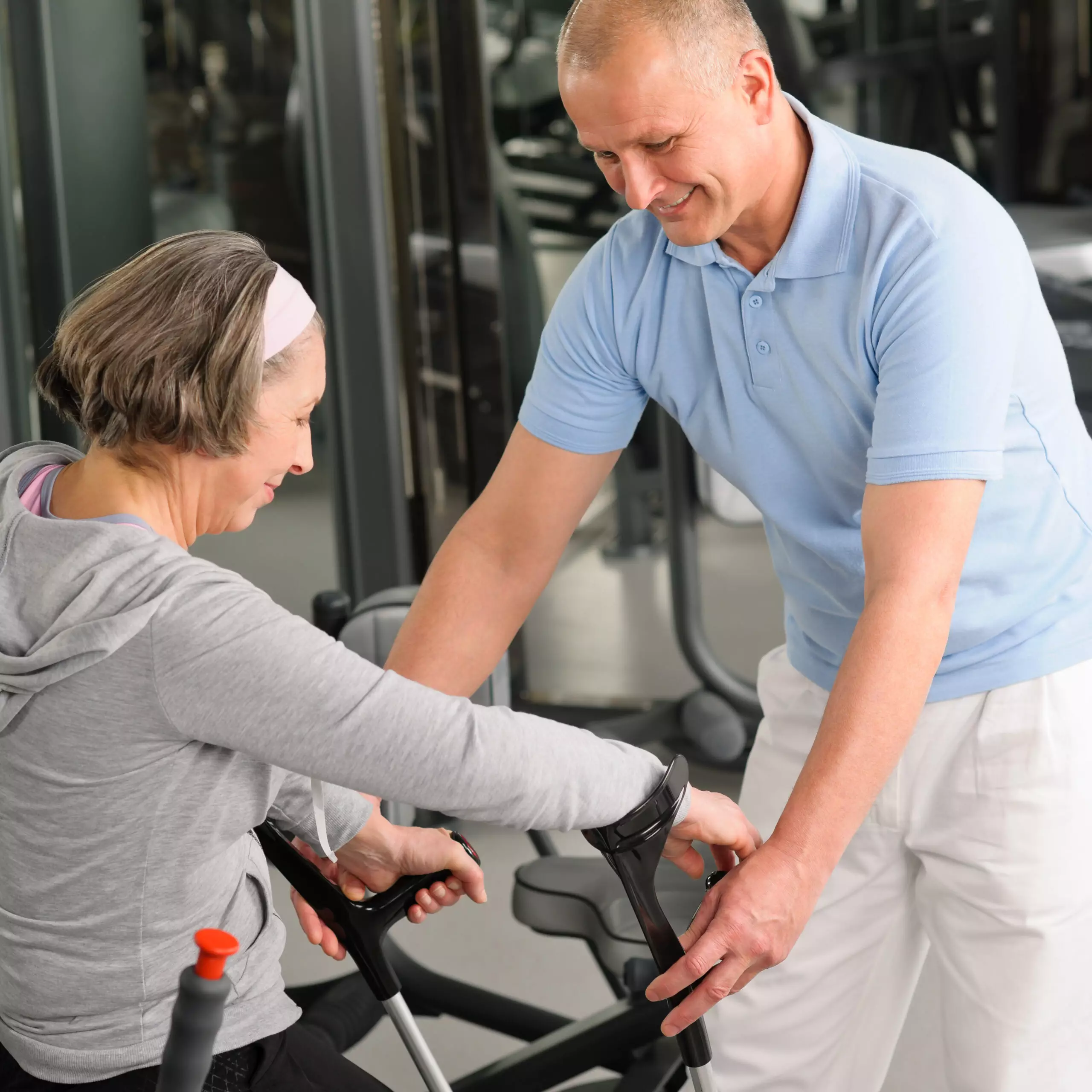 Personal trainer assisting senior woman at gym.