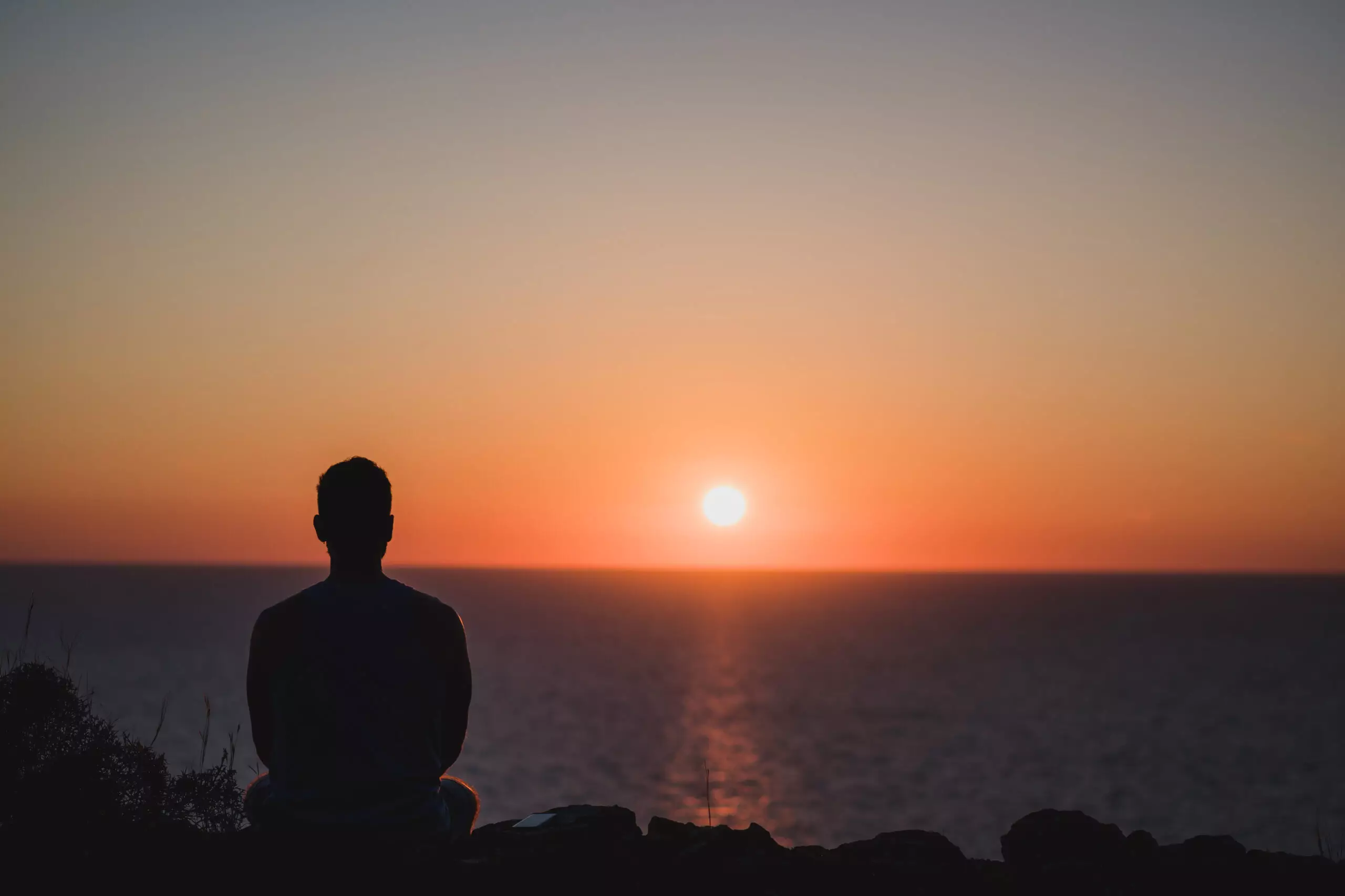 Person meditating by sea at sunset